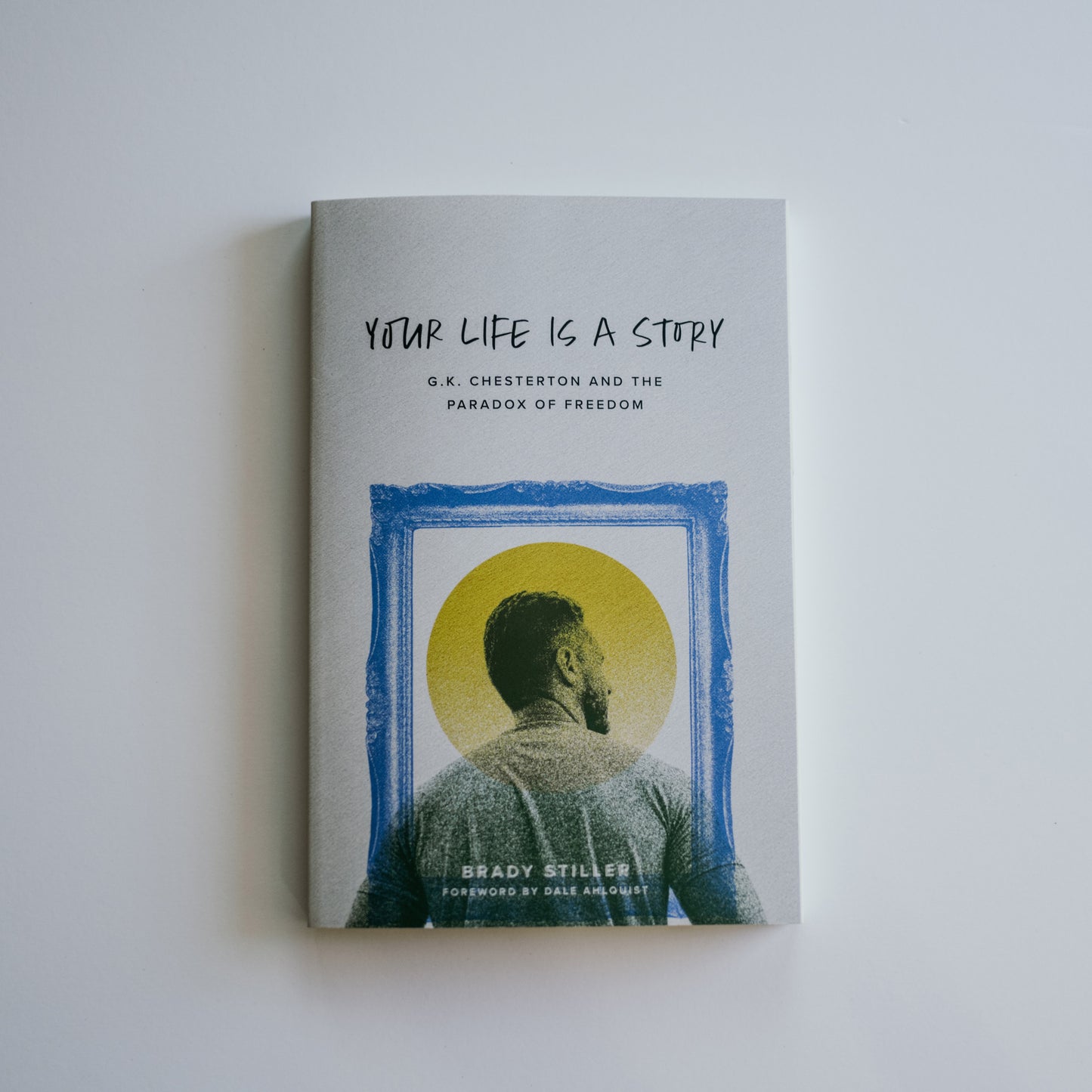 Your Life Is a Story book cover featuring a man looking at a yellow circle within a blue frame, by Brady Stiller with contributors gid://shopify/Page/97758904377 and gid://shopify/Page/97732132921, ideal for Catholic spiritual growth and evangelization.