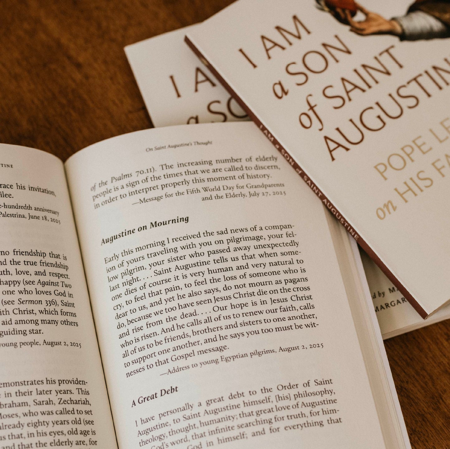 Open book displaying text on Saint Augustine's theology with two "I Am a Son of Saint Augustine" books on a table, paperback 9781685783198