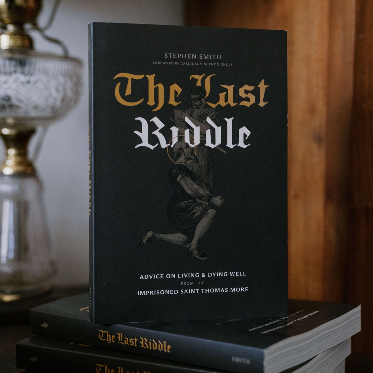 Book titled 'The Last Riddle' by Stephen Smith on a stack of books with a blurred background.
