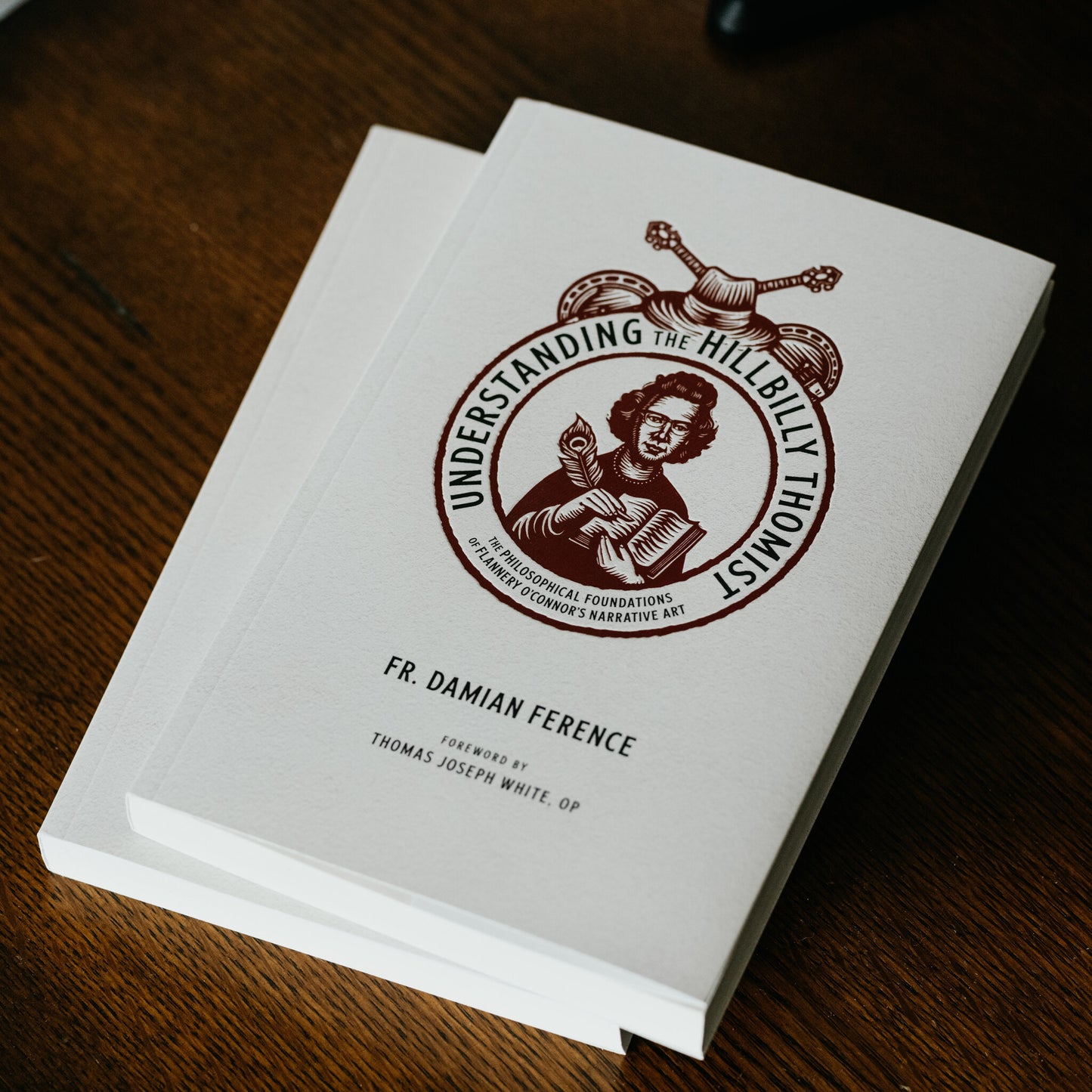 Two copies of the book Understanding the Hillbilly Thomist by Fr. Damian Ference with foreword by Thomas Joseph White on a wooden surface, The Philosophical Foundations of Flannery O’Connor’s Narrative Art, published by Word on Fire, paperback 9781685780166