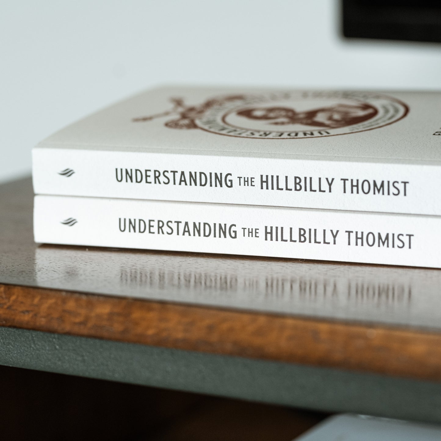 Two copies of the book Understanding the Hillbilly Thomist stacked on a wooden surface, The Philosophical Foundations of Flannery O’Connor’s Narrative Art, featuring scholarly endorsements, published by Word on Fire, paperback 9781685780166