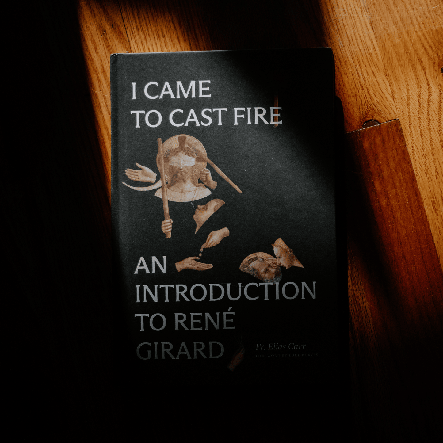 Book titled "I Came to Cast Fire: An Introduction to René Girard" by Fr. Elias Carr, shown in soft light on wooden surface, book on mimetic theory, anthropology, hardcover 9781685781668