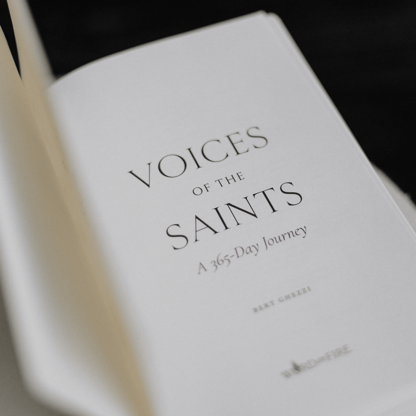 Open book page showing the title "Voices of the Saints: A 365-Day Journey" by Bert Ghezzi, published by Word on Fire, daily devotional for Catholics, hardcover 9781685781163