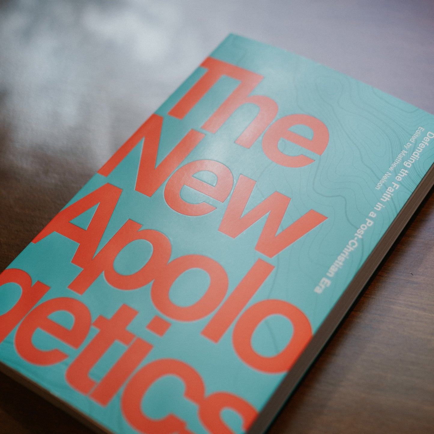 The New Apologetics book with bold orange text on a light blue cover, authored by multiple contributors including Matthew Nelson and Thomas Collins, paperback 9781685780043