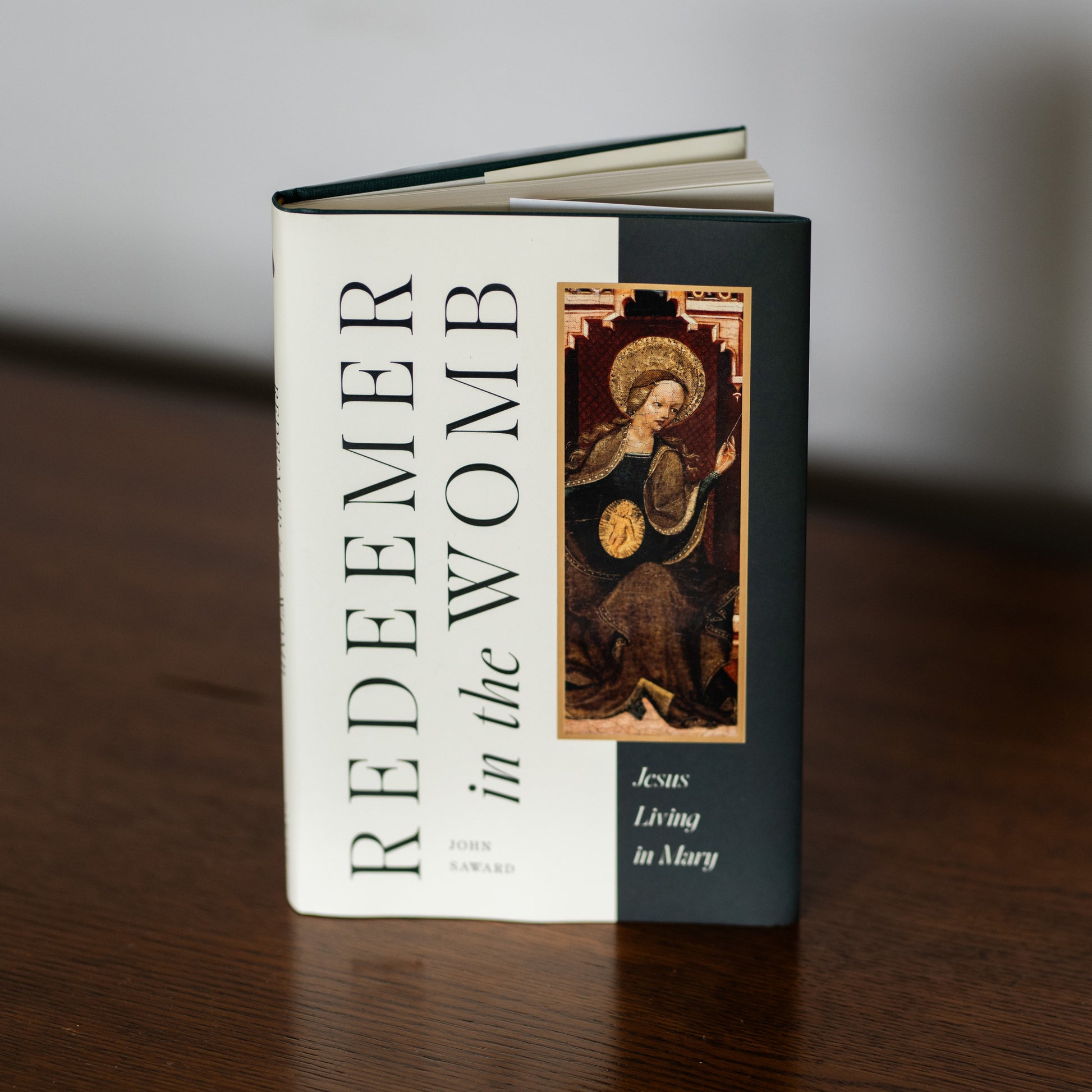 Redeemer in the Womb book standing on a wooden surface, featuring a classic religious artwork of Mary with a halo, authored by John Saward, suitable for readers interested in Catholic theology and spiritual growth, mariology, incarnation, hardcover 9781685780722