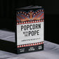 Popcorn with the Pope book standing upright with a marquee-style cover design featuring lights and a Vatican-themed graphic, by David Paul Baird, Andrew Petiprin, Michael Ward, published by Word on Fire, paperback 9781685789848