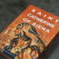 An artistic close-up of the book Saint Catherine of Siena with an orange cover featuring a painted portrait of the saint, by Father Paul Murray, OP, reflections on St. Catherine of Siena, book on Catholic female saint, hardcover 9781943243648
