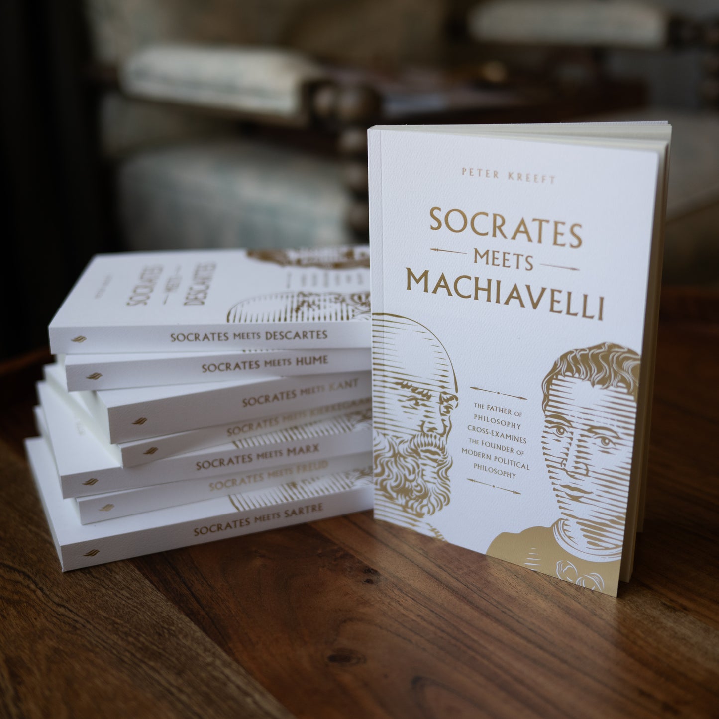 A stack of philosophical books on a wooden table featuring Socrates Meets Machiavelli in white covers with gold text, part of the Socrates Meets Box Set by contributor Peter Kreeft.