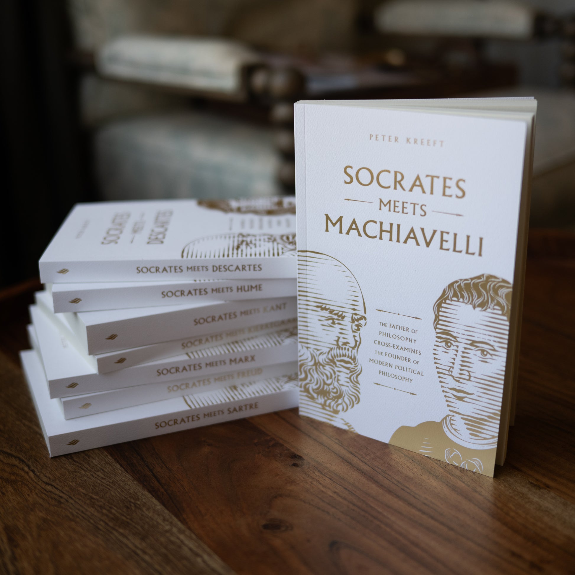 A stack of philosophical books on a wooden table featuring Socrates Meets Machiavelli in white covers with gold text, part of the Socrates Meets Box Set by contributor Peter Kreeft.
