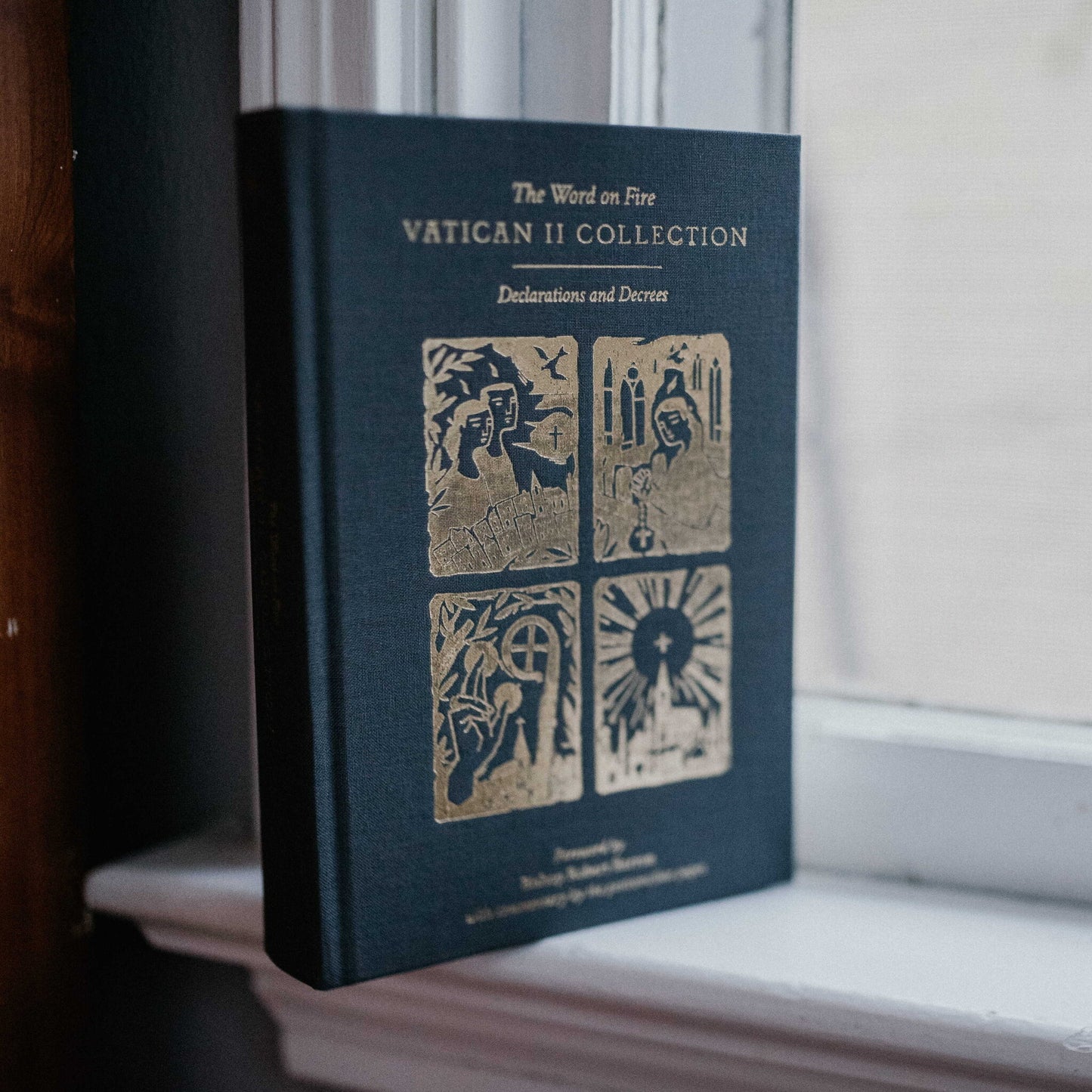 The Word on Fire Vatican II Collection: Declarations and Decrees book standing upright on a windowsill, featuring gold embossed religious imagery, foreword by Bishop Robert Barron, hardcover 9781685780135