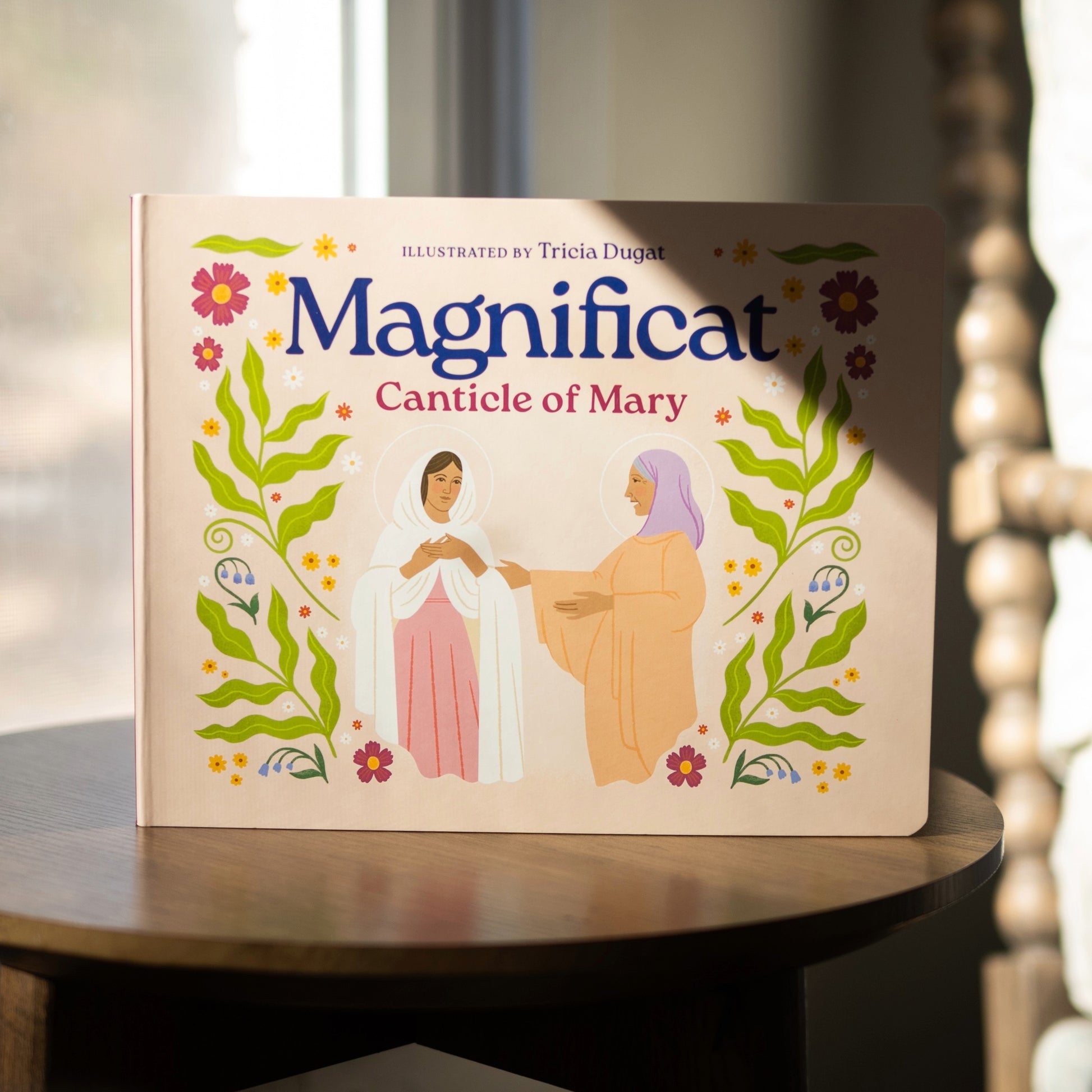 Board book titled Magnificat Canticle of Mary illustrated by Tricia Dugat, for ages 1-5, showing illustrations of Mary and her cousin Elizabeth at the Visitation, 9781685781521